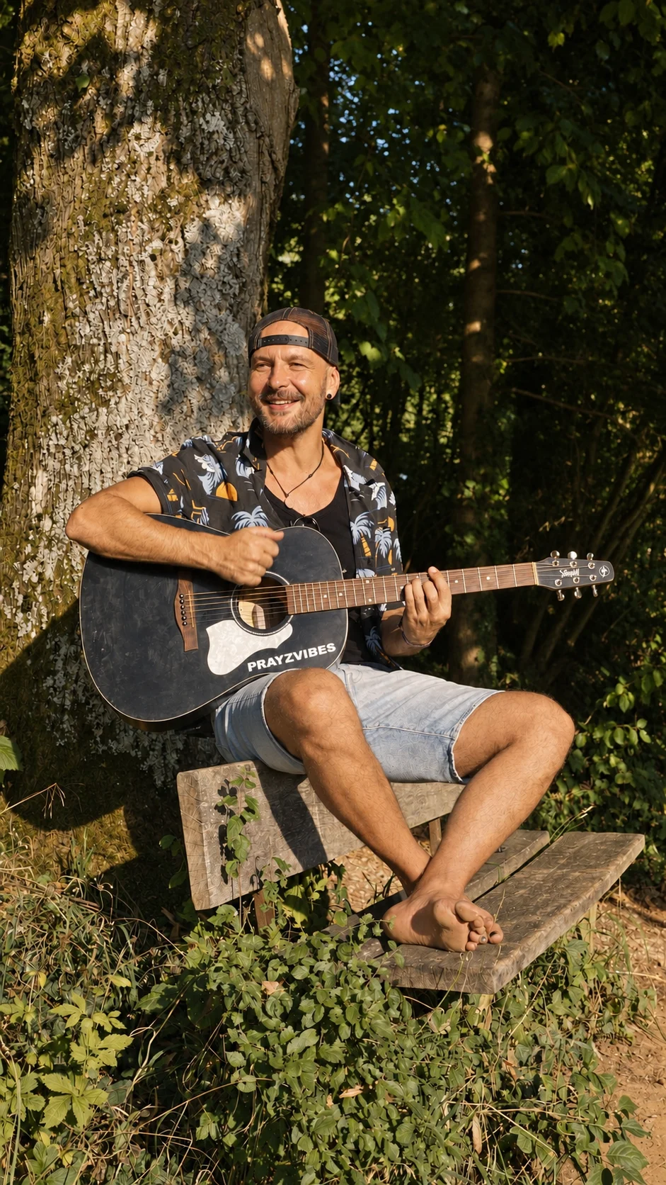 PRAYZ barefoot with his guitar by a tree — creative photographic treatment