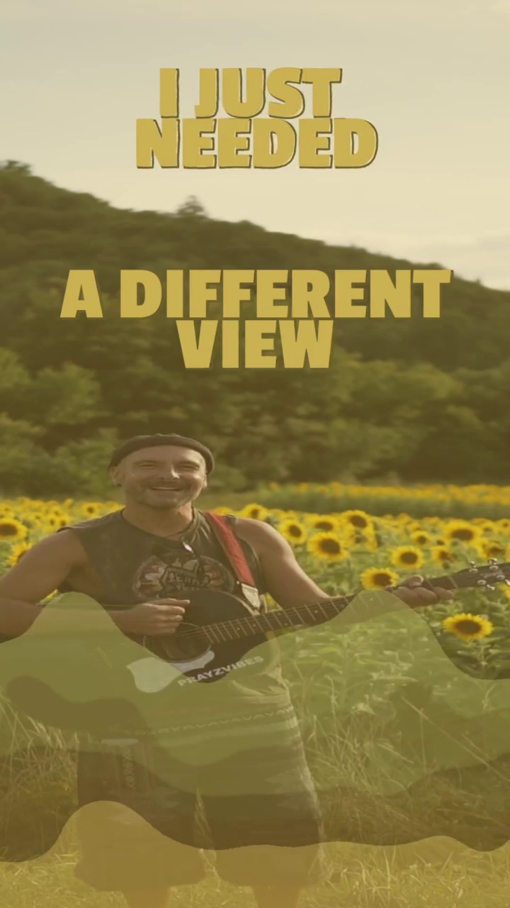 Still from the Mountain Day reel: PRAYZVIBES smiling with a black acoustic guitar in a sunflower field