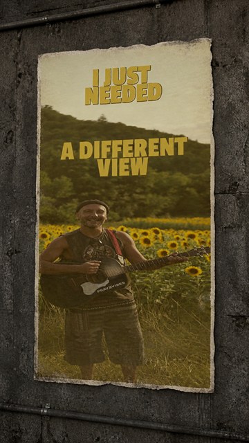 Still from the Mountain Day reel: PRAYZ smiling with a black acoustic guitar in a sunflower field
